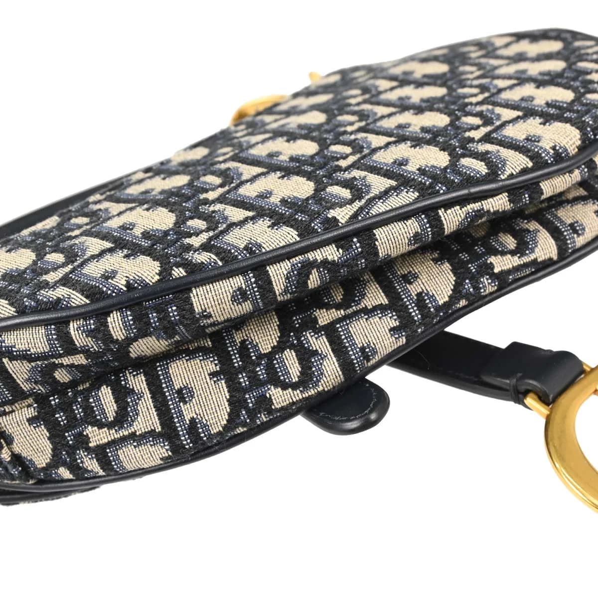Curved saddle-shaped bag in navy patterned canvas with beige trim and a strap.
