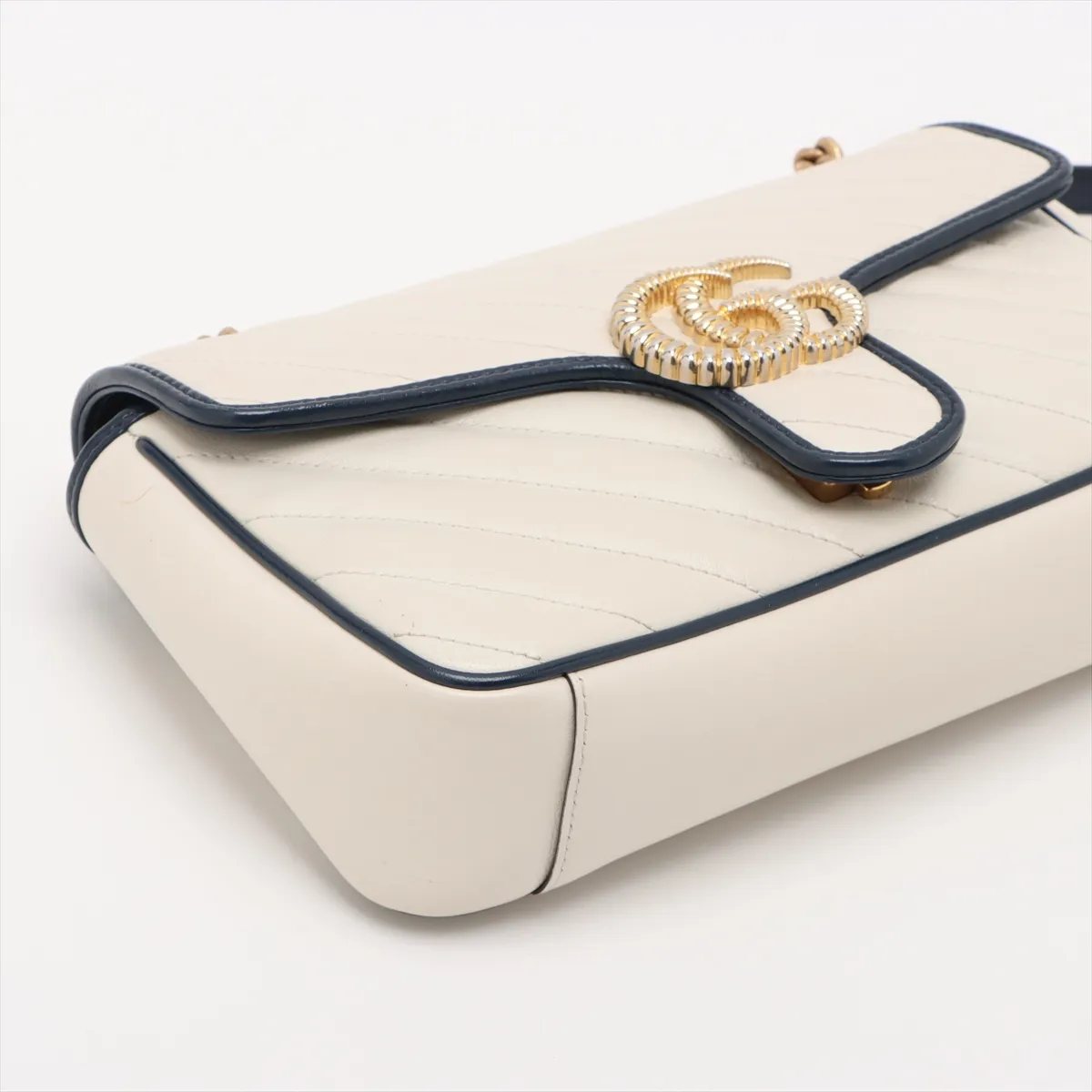White chevron-quilted leather flap bag with navy trim, a double-G clasp and a chain strap.