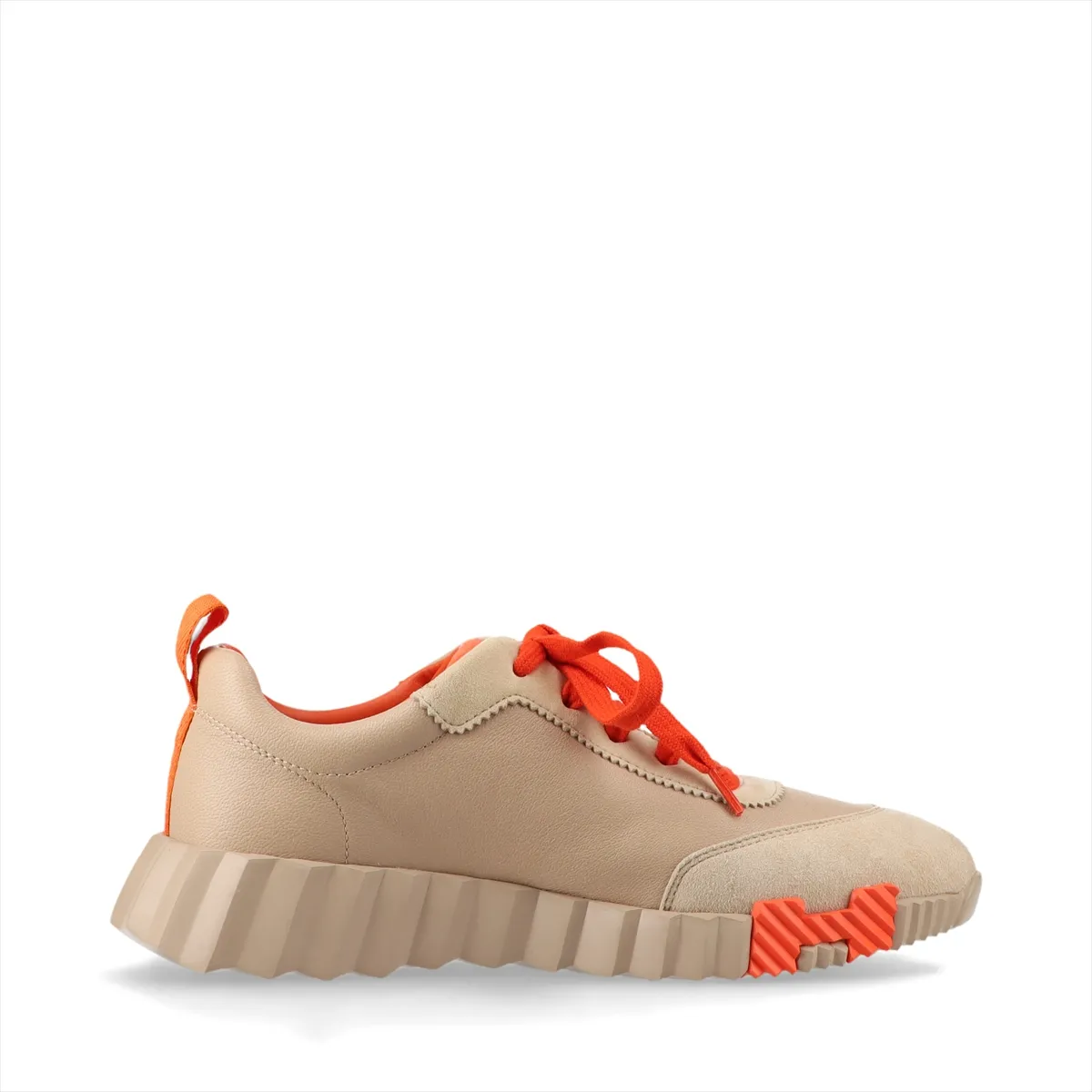 Low-top trainers in beige with orange accents, mixed smooth and napped panels, on a plain background.