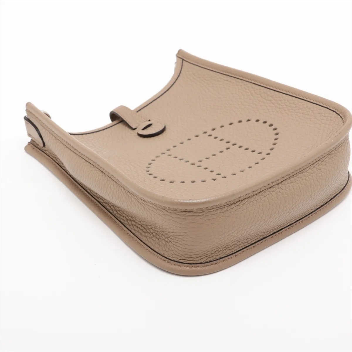 Small beige leather shoulder bag with perforated H on the front and a long woven strap.