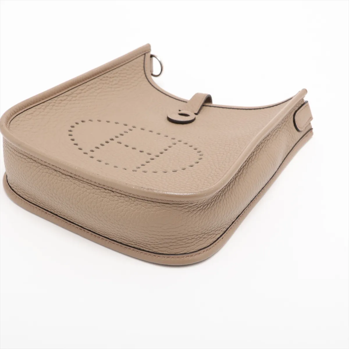 Small beige leather shoulder bag with perforated H on the front and a long woven strap.