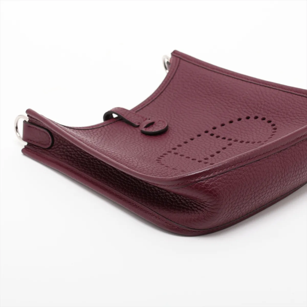 Small deep red leather shoulder bag with perforated H on the front and a long woven strap.