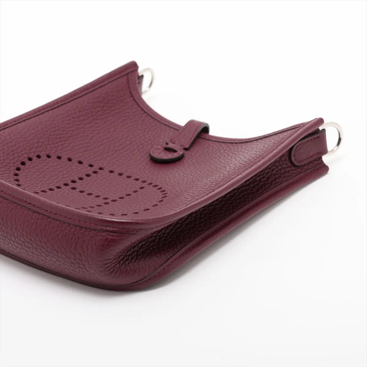 Small deep red leather shoulder bag with perforated H on the front and a long woven strap.