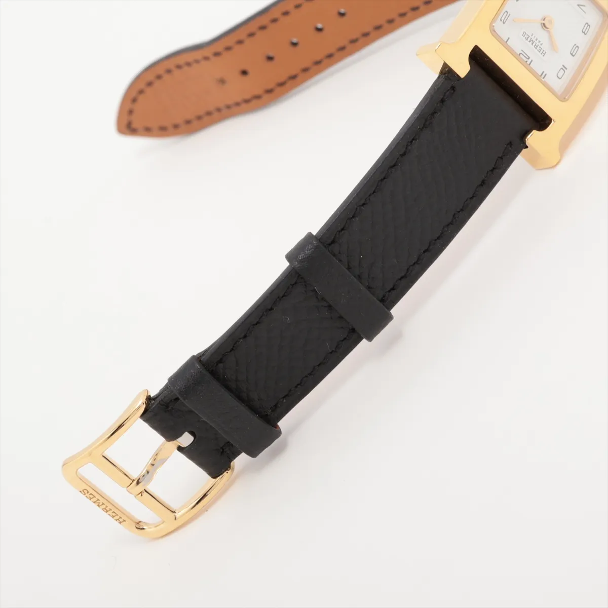 Square gold-tone watch case with white dial and slim leather strap.