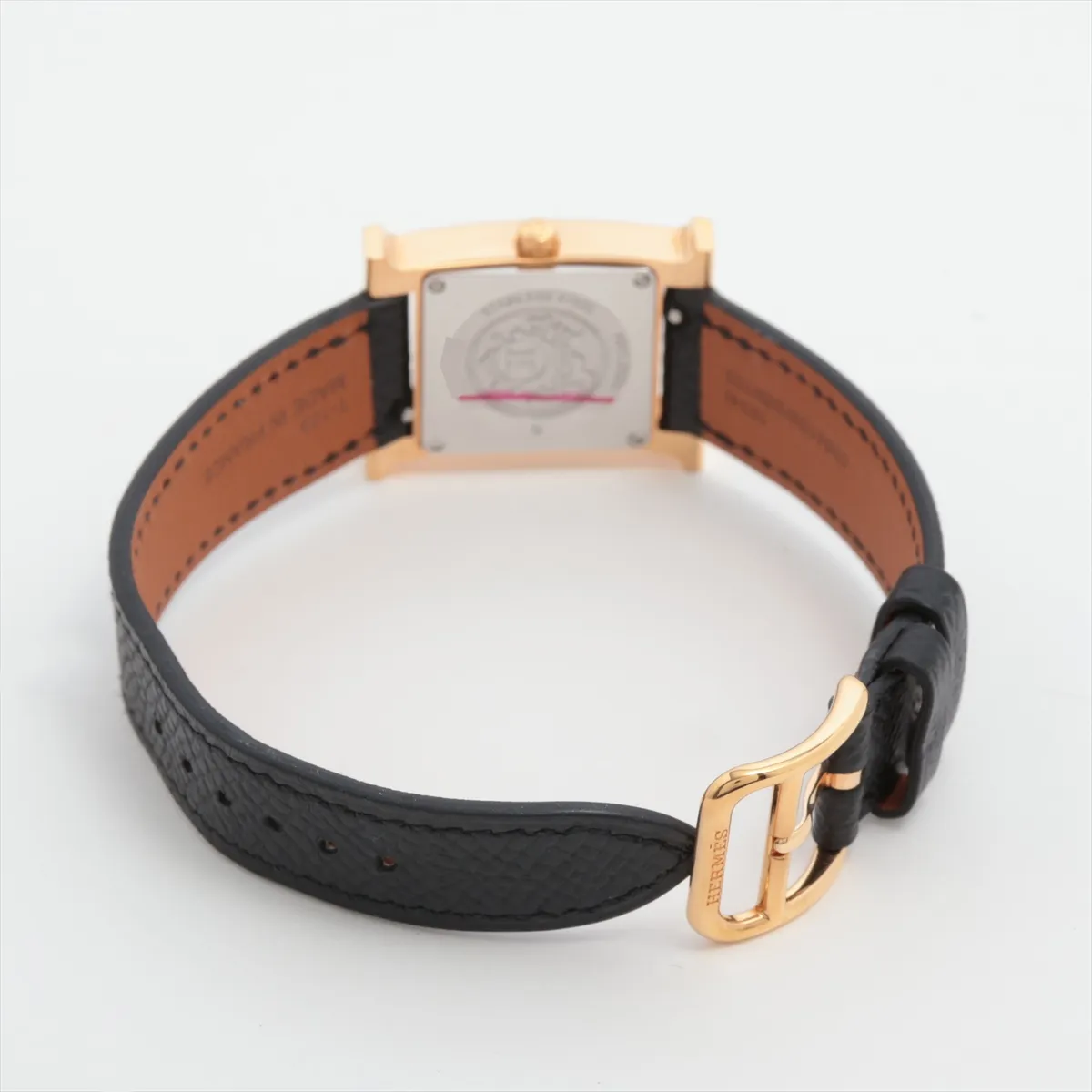 H-shaped gold-toned watch case with pale shell dial on a leather strap.