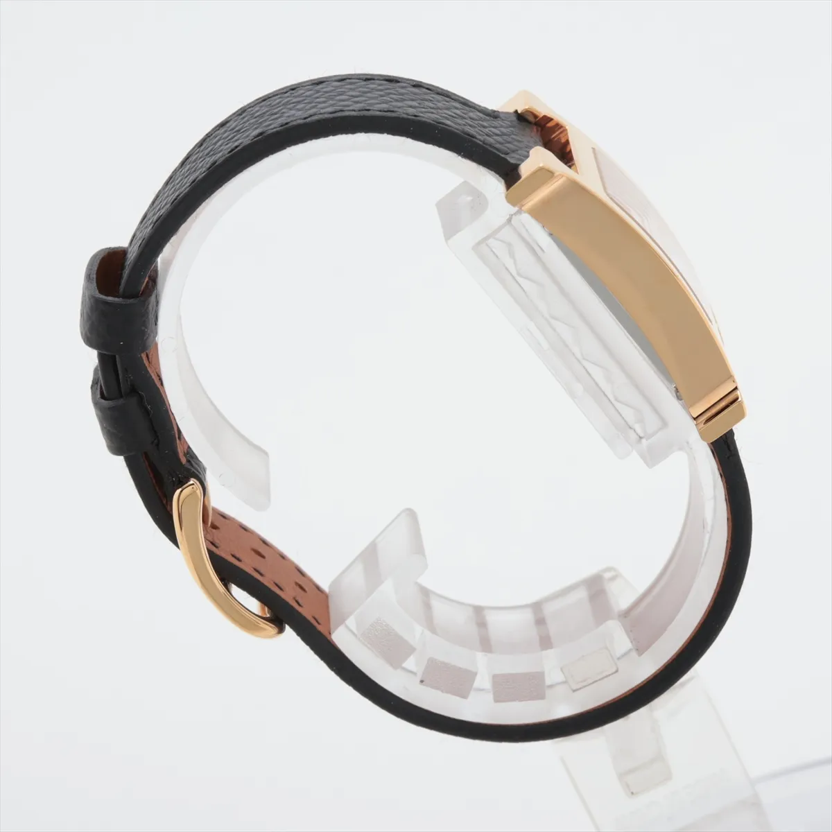 H-shaped gold-toned watch case with pale shell dial on a leather strap.