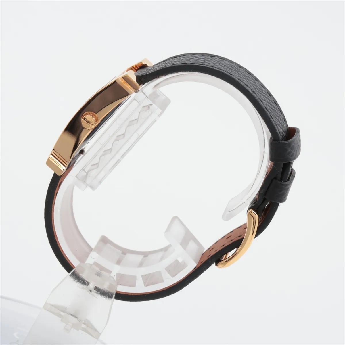 H-shaped gold-toned watch case with pale shell dial on a leather strap.