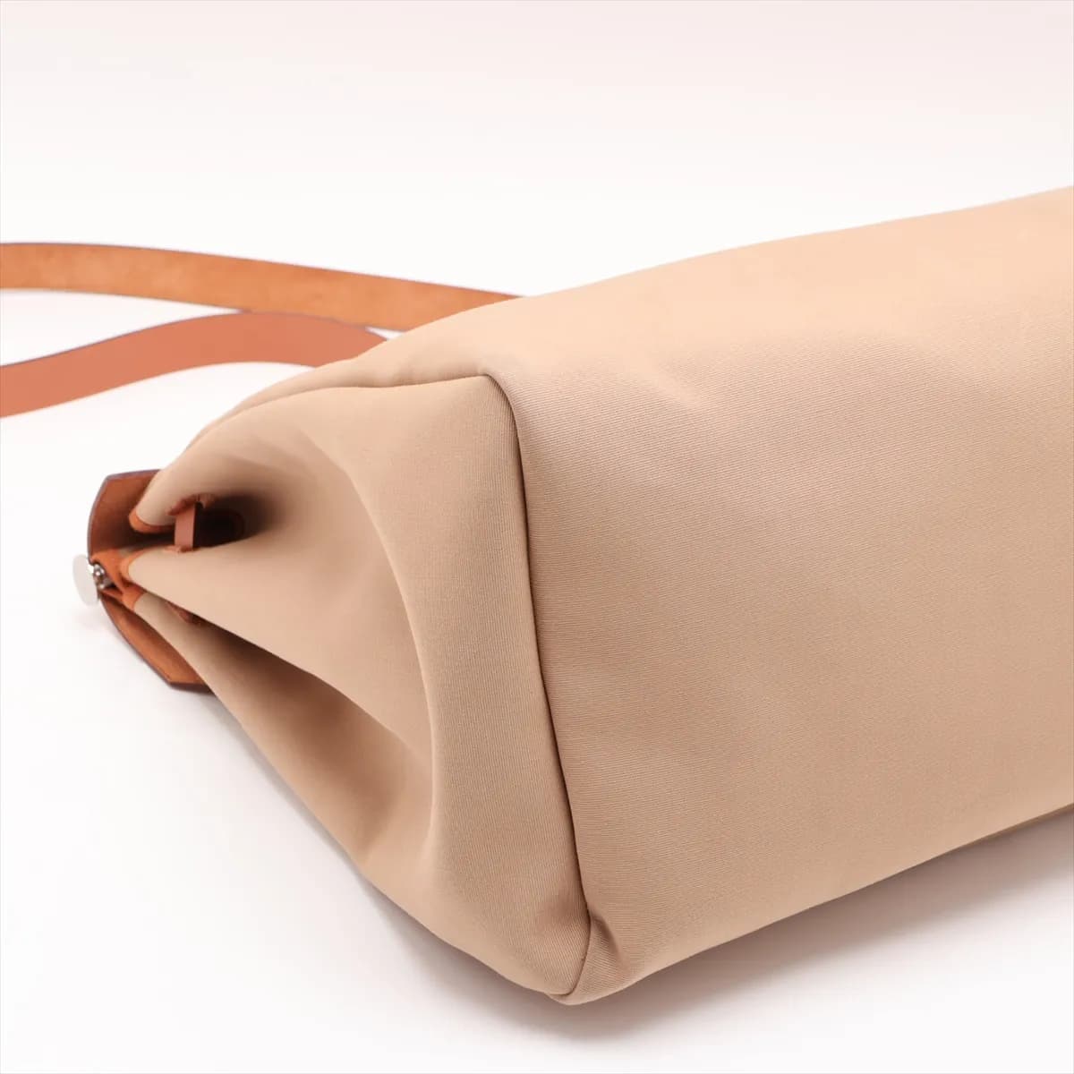 Beige canvas bag with tan leather flap and trim, front strap closure and a shoulder strap.