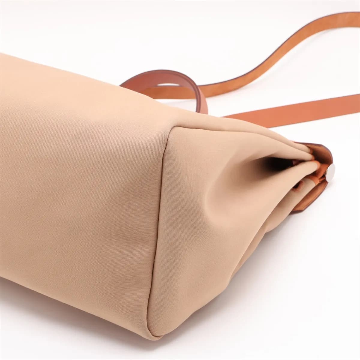 Beige canvas bag with tan leather flap and trim, front strap closure and a shoulder strap.