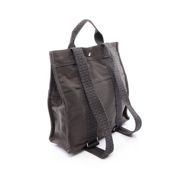Product photograph of a grey patterned canvas backpack with a flap closure.