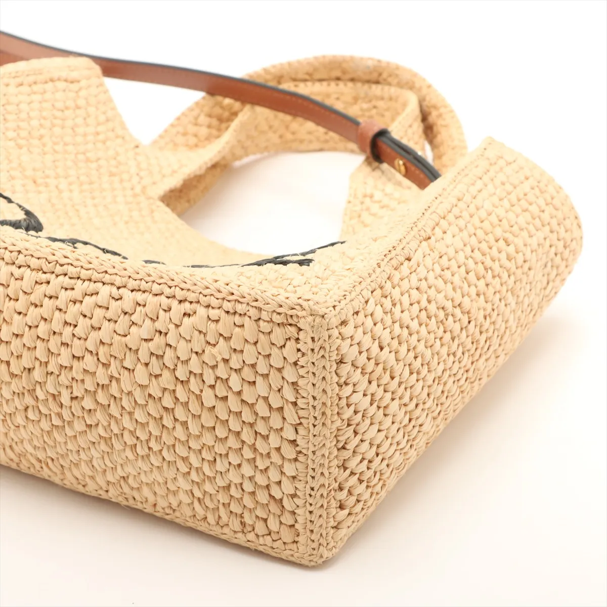 Beige woven raffia tote with leather handles and a lettered logo across the front