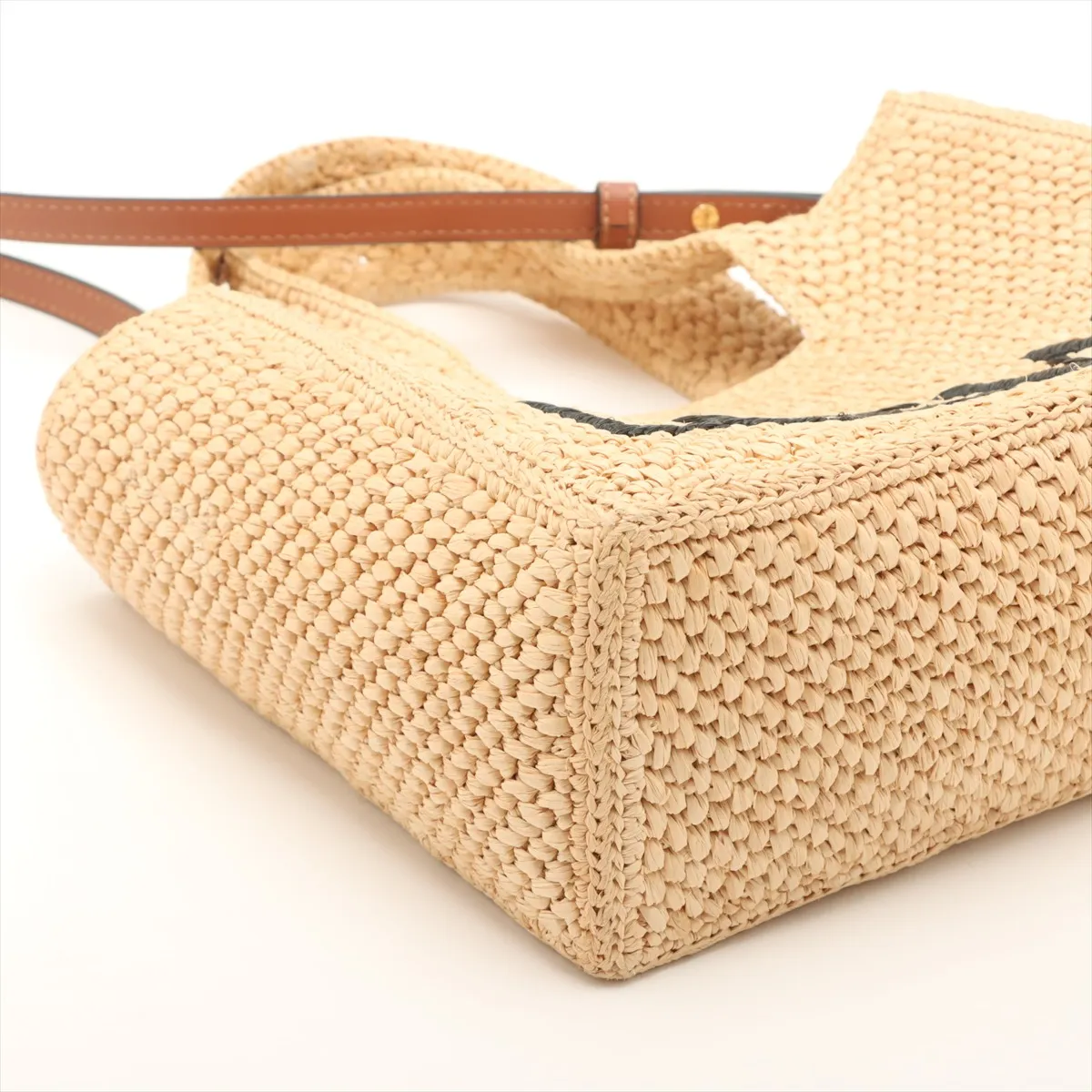 Beige woven raffia tote with leather handles and a lettered logo across the front
