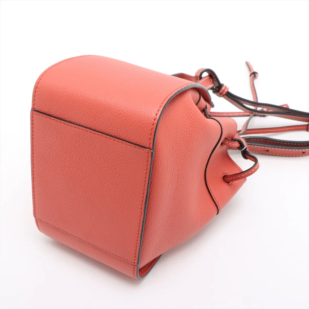 Orange leather bucket-style handbag with drawstring top and a detachable shoulder strap.