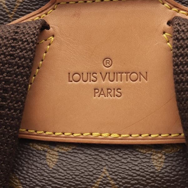 Brown monogram-patterned canvas backpack with leather straps and buckled flap pockets.