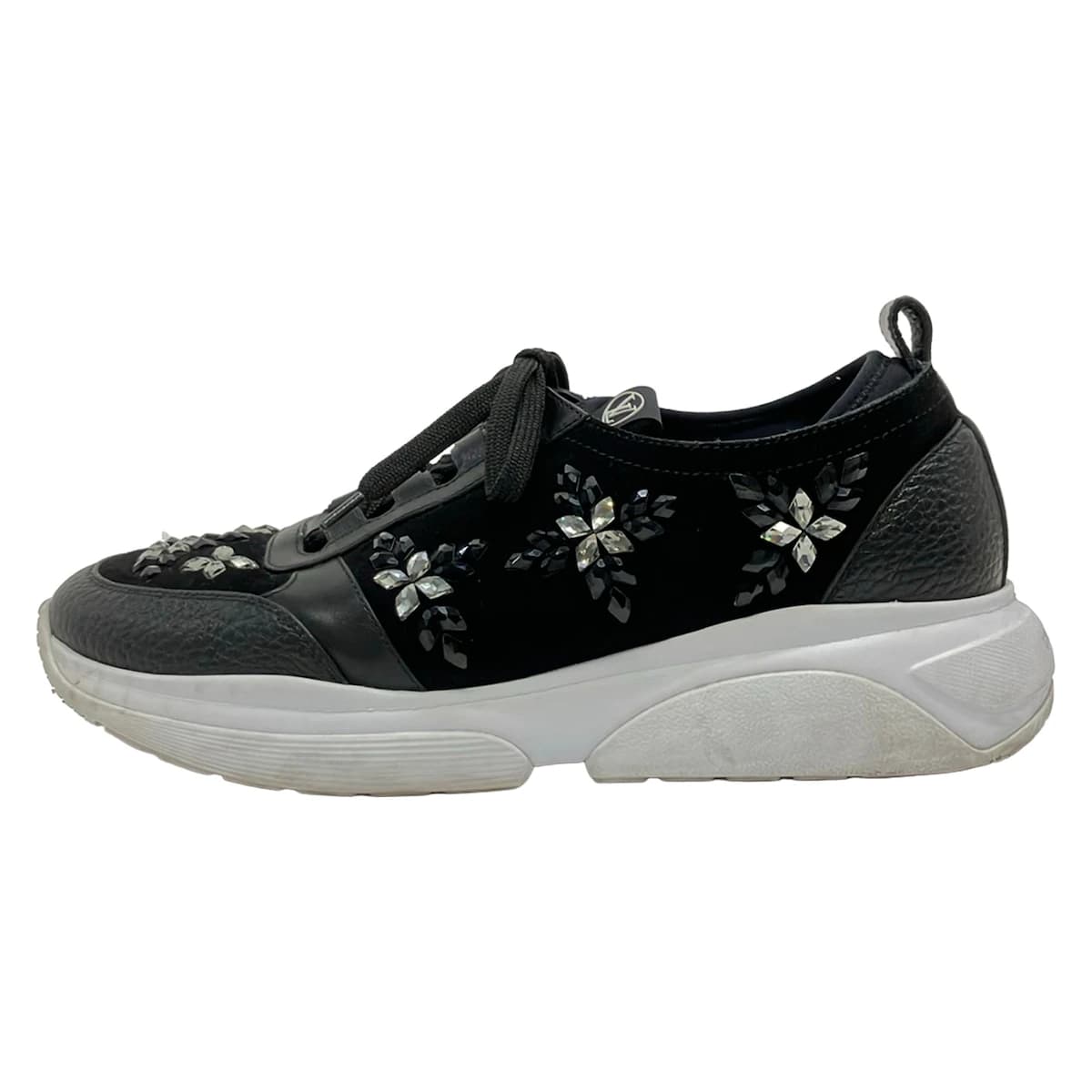 Black shoe with transparent panels and sparkling jewel trim, on a plain background.