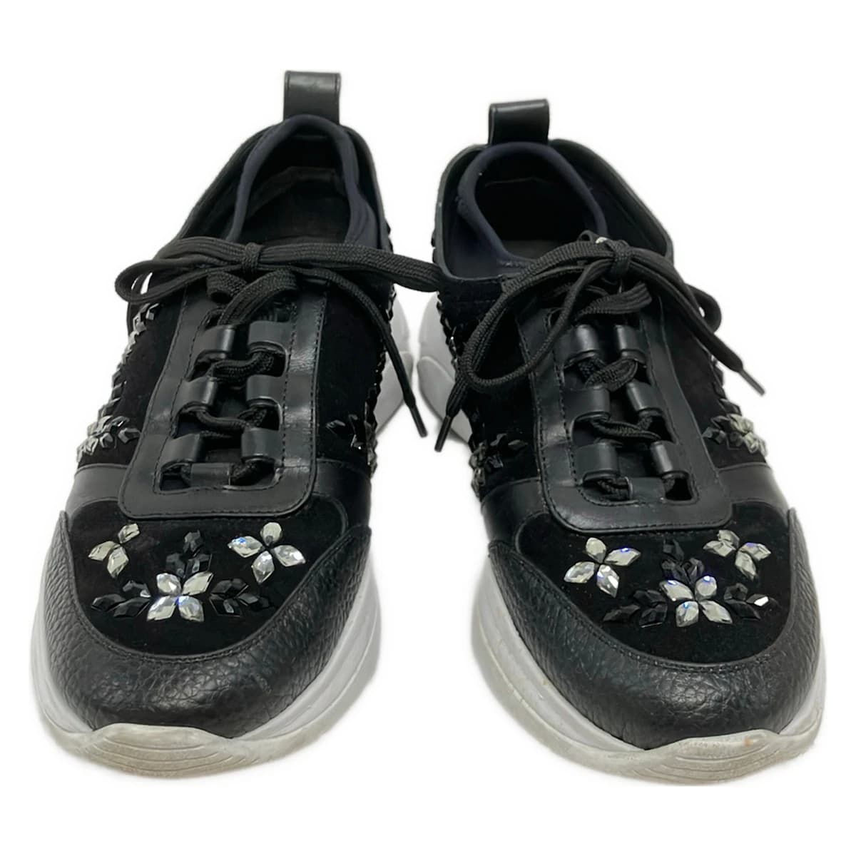 Black shoe with transparent panels and sparkling jewel trim, on a plain background.