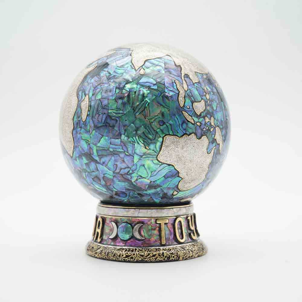Product photograph of a small rounded vinyl figure with iridescent shell inlay decoration.