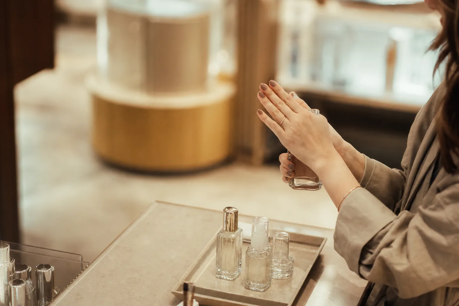 Hands pressing a small glass skincare bottle between palms at a pale department store beauty counter